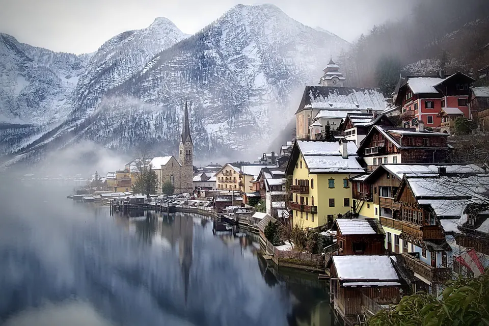 Zasněžený Hallstatt s kostelní věží a mlhou nad jezerem Hallstättersee v zimě